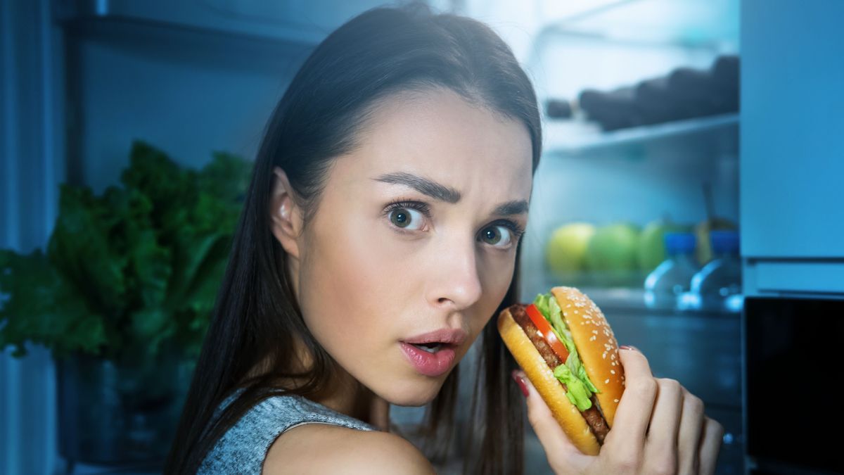 Young,Woman,Eating,Burger,From,Fridge,At,Night,Kitchen.,Diet