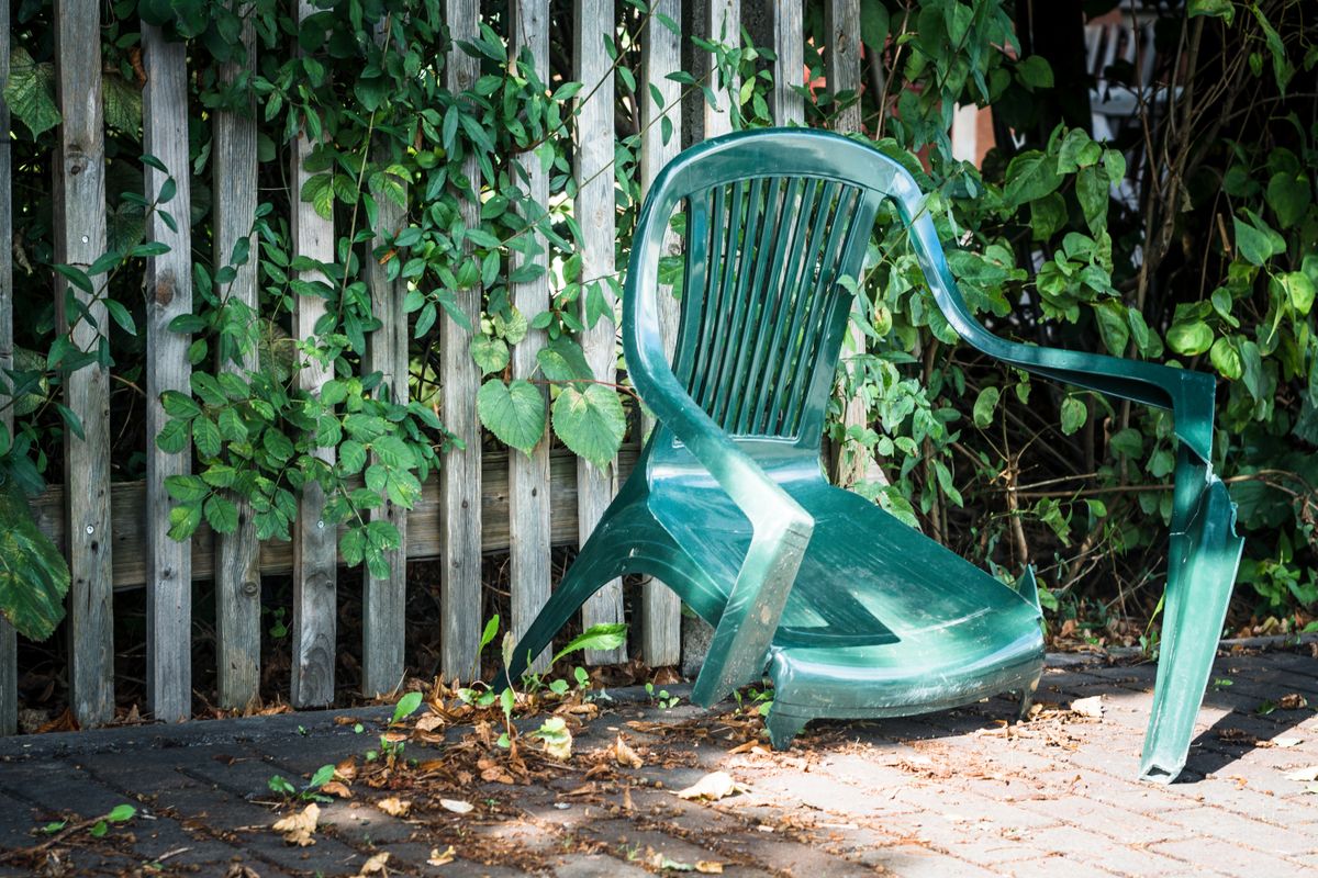 A,Broken,Green,Garden,Chair,In,Front,Of,A,Fence