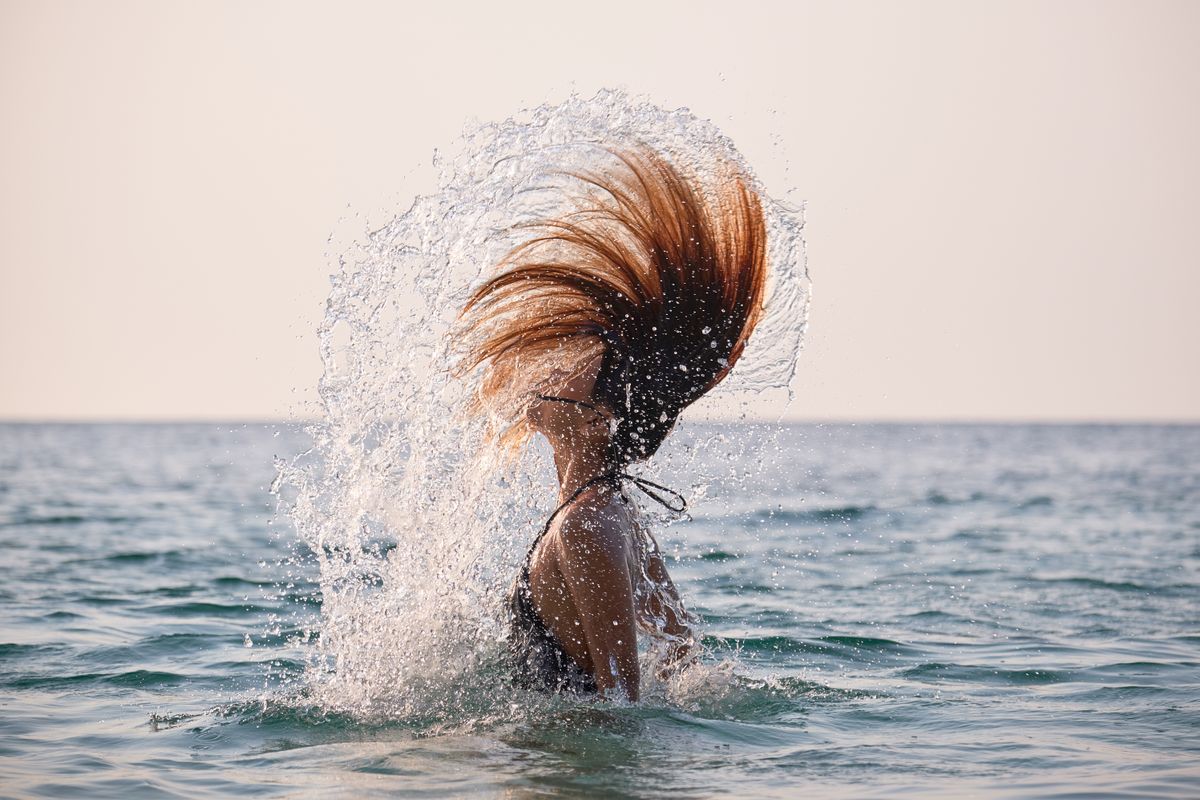 Asian woman doing a water spin with her hair in the ocean during sunset .