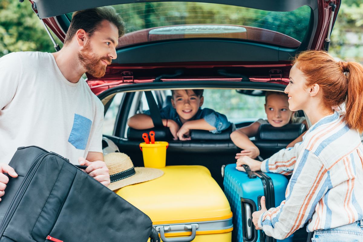 Young,Parents,Packing,Luggage,In,Trunk,Of,Car,With,Kids